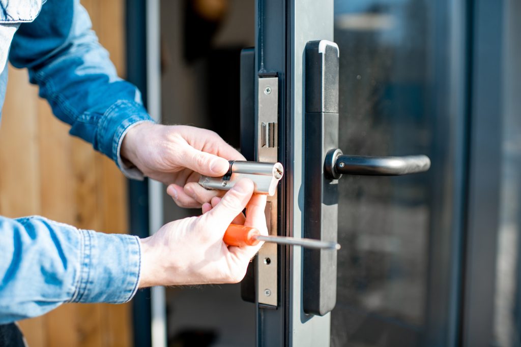 Homme changeant le noyau d'une serrure de porte de la porte vitrée d'entrée, vue rapprochée sans visage - Service de serrurier professionnel